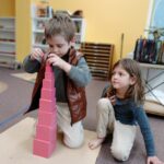 Two students focused on building the pink tower in a Montessori classroom