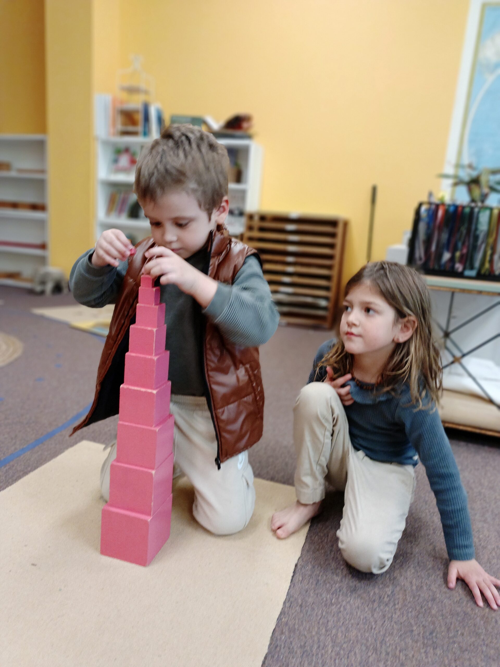 Two students focused on building the pink tower in a Montessori classroom